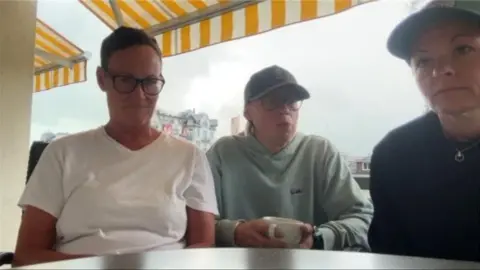 Three woman sit at a table on a video conference call.