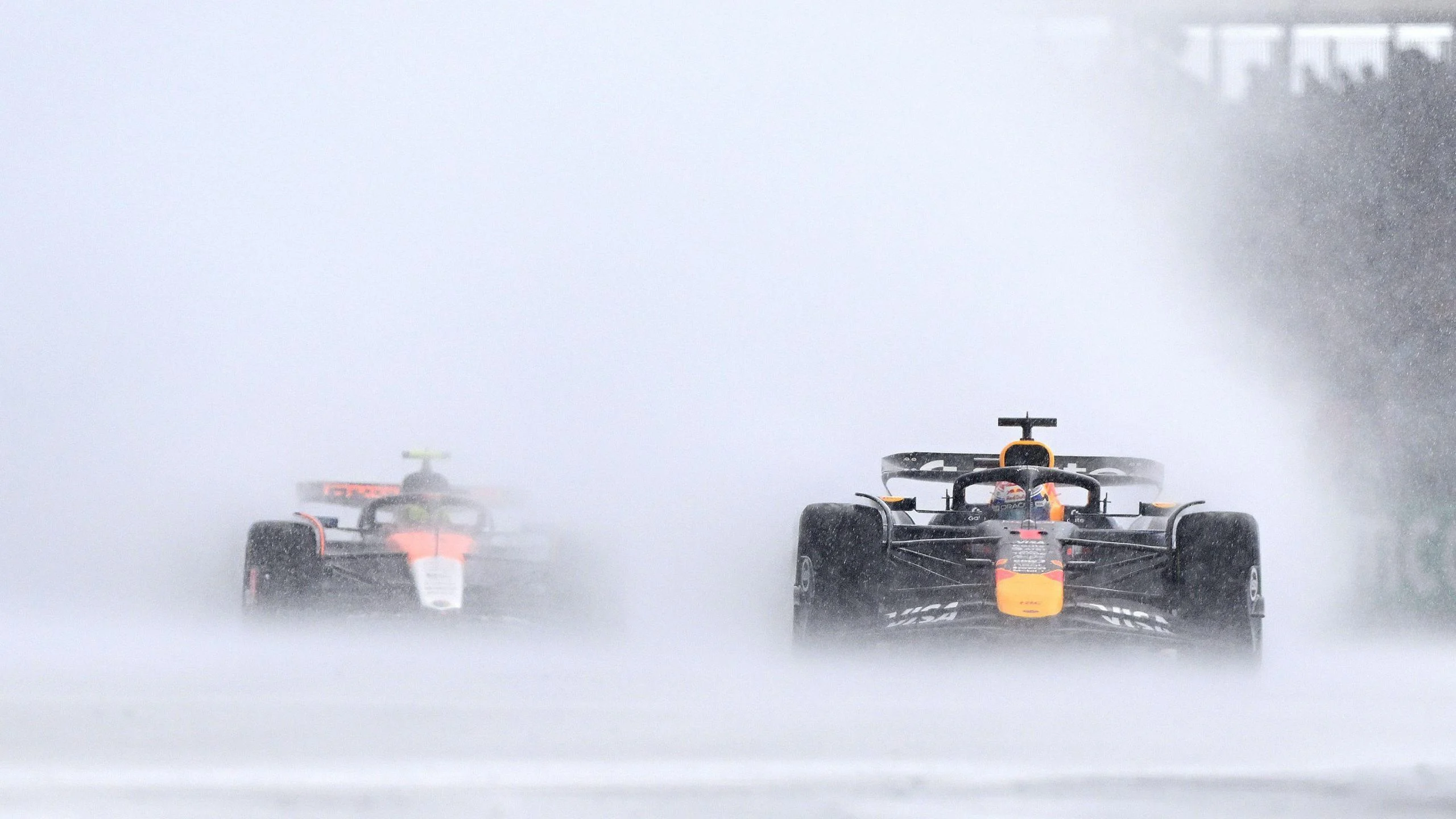 Red Bull's Max Verstappen with McLaren's Lando Norris in the background, with both cars throwing up spray during a torrential downpour during the 2025 British Grand Prix