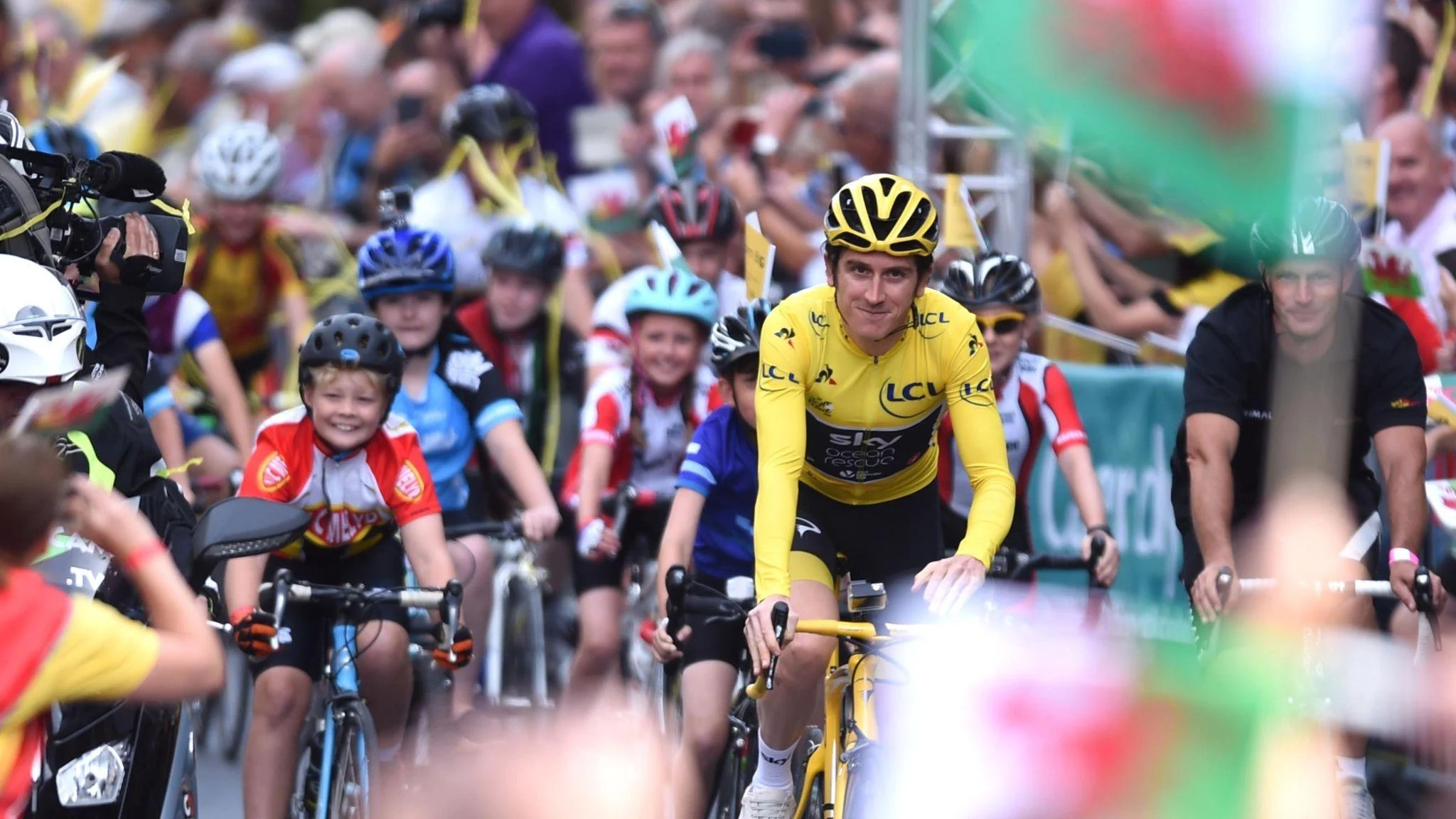 Geraint Thomas in a yellow jersey rides through the crowds along with youngsters