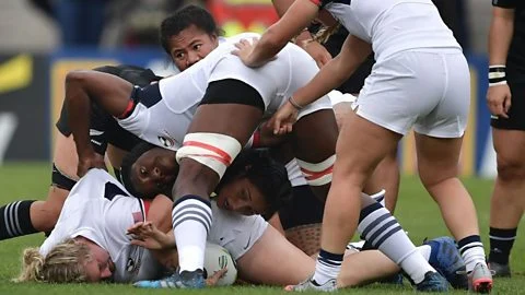 Rugby players from New Zealand and USA form a ruck over the ball on the ground in a women's rugby match
