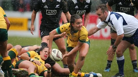 A female Australian rugby player collects and passes the ball out of a ruck