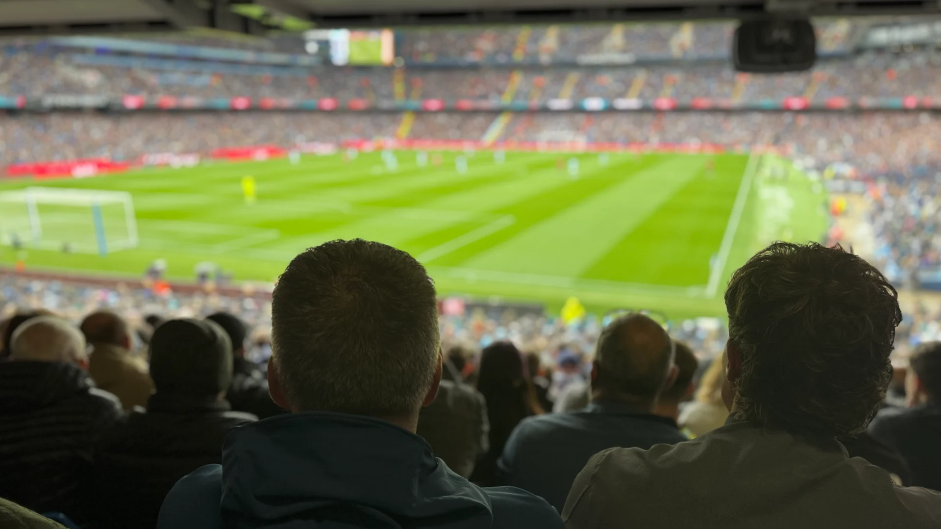 A photo from the North Stand of the Ethiad Stadium with the match ongoing on the pitch in the background and fan's heads in the foreground.